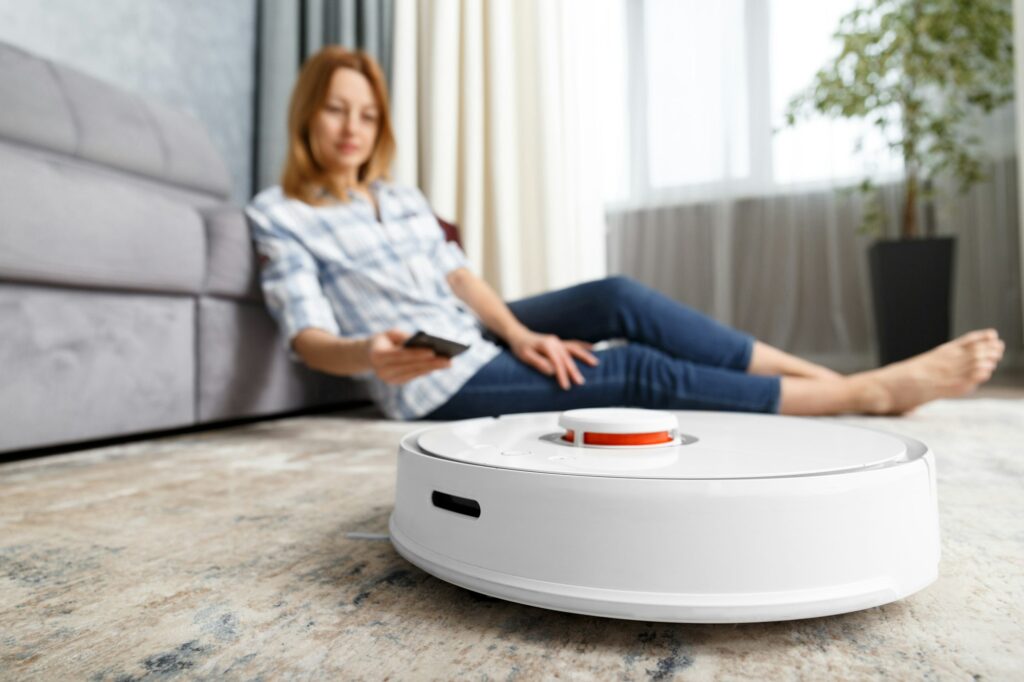 The girl sits on the floor and controls the robot vacuum cleaner using a smartphone, smart home.